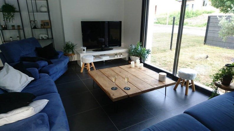 Puede incluir: Una sala de estar con un sof&aacute; seccional azul, una mesa de caf&eacute; de madera grande con dos copas de champ&aacute;n y un taburete blanco. La habitaci&oacute;n tiene una ventana grande con vista a un c&eacute;sped verde y una cerca negra.