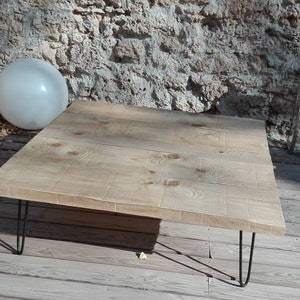 Puede incluir: Una mesa de centro de madera clara con una tapa rectangular y patas de horquilla negras. La mesa est&aacute; sobre una plataforma de madera.