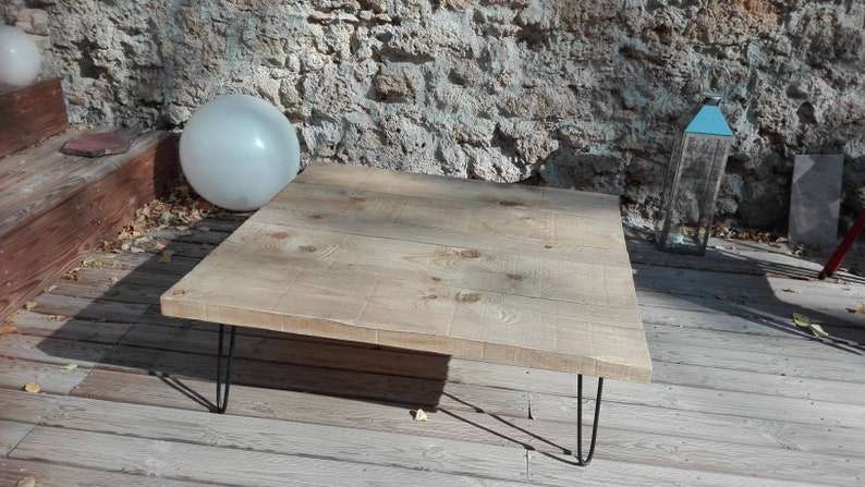 Puede incluir: Una mesa de centro de madera clara con una tapa rectangular y patas de horquilla negras. La mesa est&aacute; sobre una plataforma de madera.