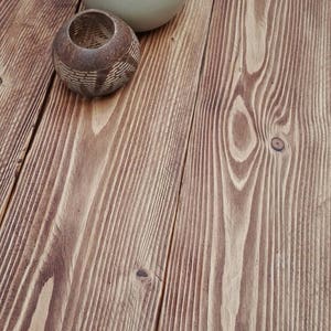 May include: A round, wooden table with a natural finish. Two decorative candle holders sit on the table. One is a light beige, round shape, and the other is a small, brown, carved container.