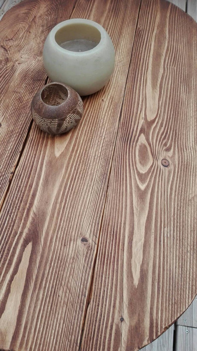 May include: A round, wooden table with a natural finish. Two decorative candle holders sit on the table. One is a light beige, round shape, and the other is a small, brown, carved container.