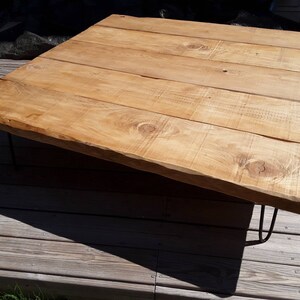 Puede incluir: Una mesa de centro de madera r&uacute;stica con un acabado de madera natural y un dise&ntilde;o de borde vivo. La mesa tiene una tapa rectangular y est&aacute; soportada por cuatro patas de metal negro en forma de horquilla.