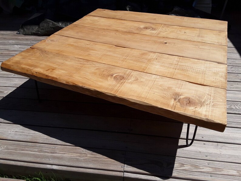 Puede incluir: Una mesa de centro de madera r&uacute;stica con un acabado de madera natural y un dise&ntilde;o de borde vivo. La mesa tiene una tapa rectangular y est&aacute; soportada por cuatro patas de metal negro en forma de horquilla.