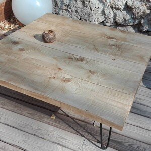 Puede incluir: Una mesa de centro de madera clara con un acabado natural. La mesa tiene una tapa cuadrada y est&aacute; sostenida por cuatro patas de horquilla negras.