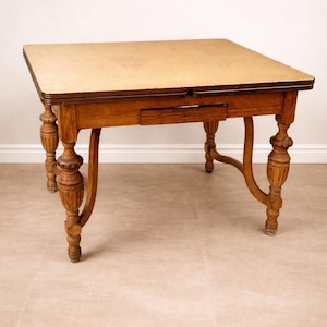 May include: A vintage wooden table with a light-colored top and ornate, carved legs. The table has a drawer and a dark brown trim around the edges. The legs are curved and have a detailed, turned design.