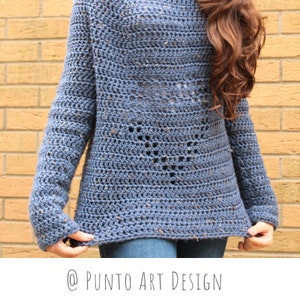 Może przedstawiać: Niebieski sweter wykonany na szydełku z fakturowanym wzorem i ażurowym designem. Sweter ma długie rękawy i luźny krój.