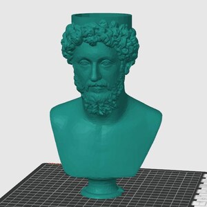 Può includere: Un busto turchese di un uomo con barba e capelli ricci, che ricorda le sculture classiche. Il busto è posto su una superficie nera a griglia, forse stampato in 3D. È un oggetto decorativo.