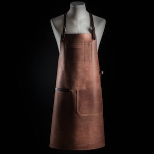 May include: A brown leather apron with adjustable straps and a large pocket. The apron is made of high-quality leather and is perfect for protecting your clothes while you work.