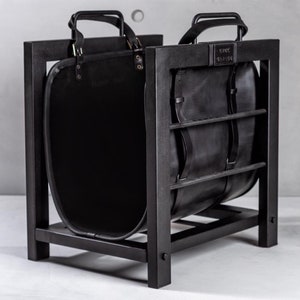 May include: Black metal log holder with a black leather log basket. The basket has two handles and the text "KNUX TANNER" is printed on the front.