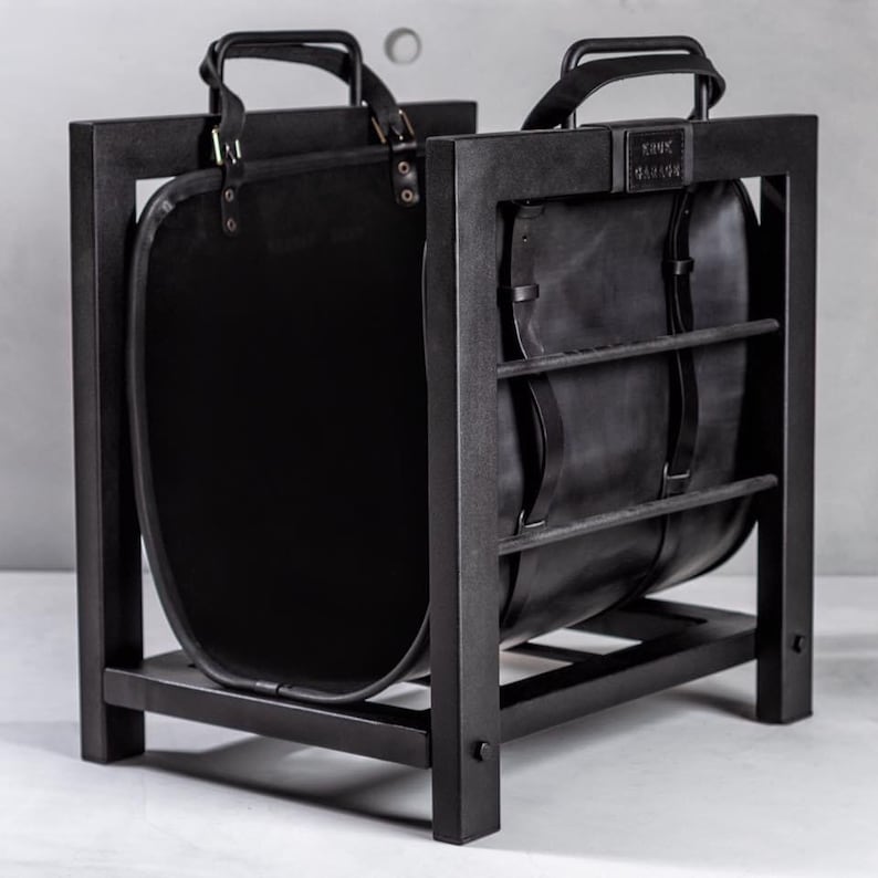 May include: Black metal log holder with a black leather log basket. The basket has two handles and the text "KNUX TANNER" is printed on the front.