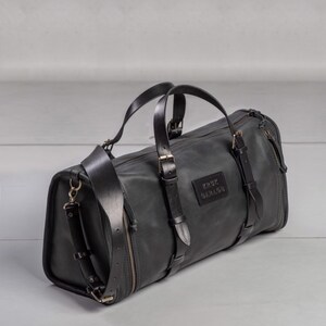 May include: Black leather duffel bag with multiple straps and buckles. The bag has a zipper closure and a label that reads "KRUX GARAGE".