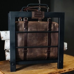 May include: A black metal log rack with a brown leather bag inside. The bag has a metal buckle and the text "SOUL TRAVELER" on the front.