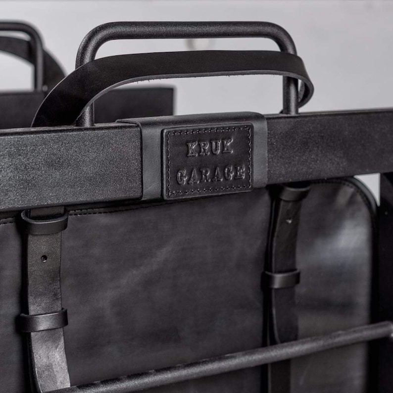 May include: Black leather backpack with a metal frame and a leather handle. The backpack has a black leather patch with the text "KRUK GARAGE" on it.