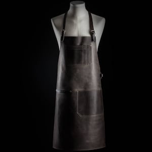 May include: A brown leather apron with adjustable straps and multiple pockets. The apron has a dark brown color and a distressed look.