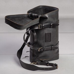 May include: A black leather backpack with multiple straps and buckles. The backpack has a large main compartment and a smaller zippered pocket on the front. The backpack is made of high-quality leather and has a vintage look.