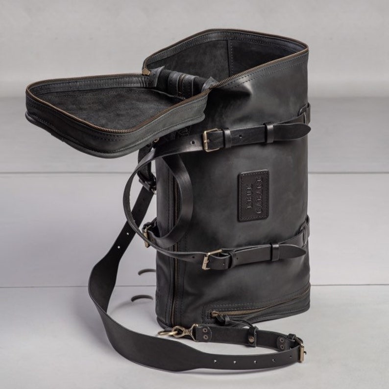 May include: A black leather backpack with multiple straps and buckles. The backpack has a large main compartment and a smaller zippered pocket on the front. The backpack is made of high-quality leather and has a vintage look.