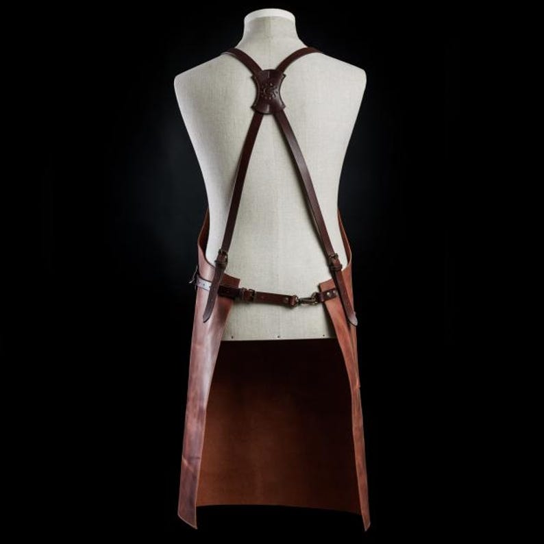 May include: A brown leather apron with adjustable straps and a long bib. The apron is made of thick, durable leather and has a classic design.