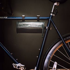 May include: A black bicycle with a black leather handlebar bag that says "Keep Garage" on it. The bicycle has a black frame and a black seat.