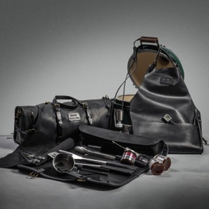 May include: A black leather grilling set with a large green and black grill, a leather apron, a leather duffel bag, a leather tool roll, and a set of grilling tools.