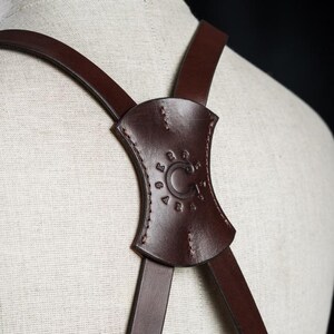 May include: Brown leather straps with a brown leather adjustable buckle. The buckle has the text "C.C. LOGAN 1915" embossed on it.