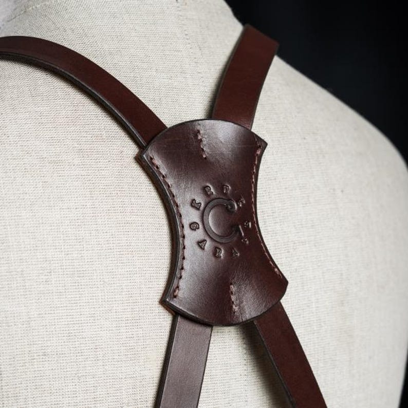 May include: Brown leather straps with a brown leather adjustable buckle. The buckle has the text "C.C. LOGAN 1915" embossed on it.