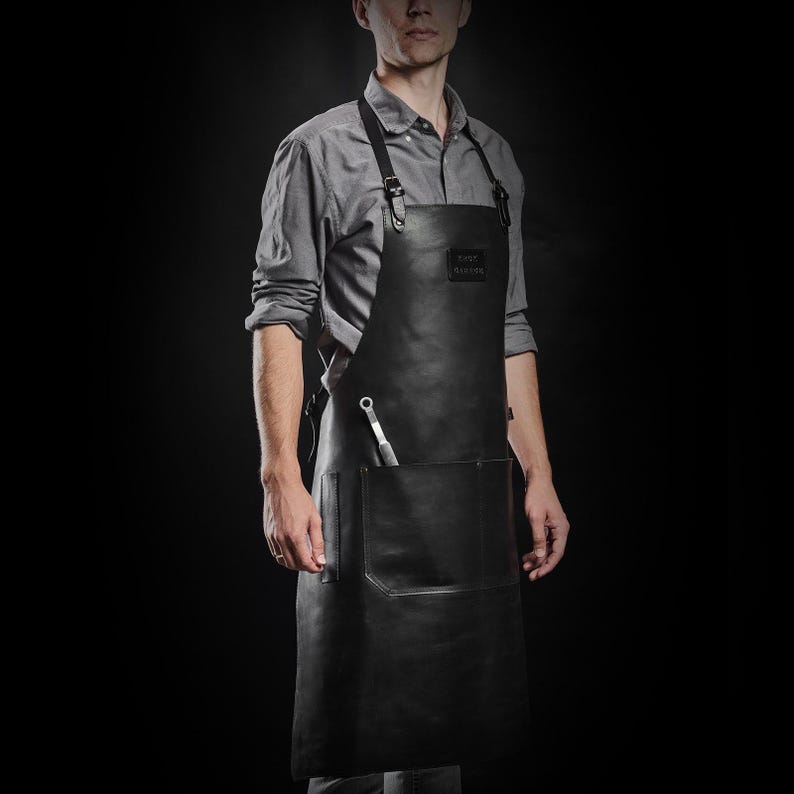 May include: A black leather apron with a large pocket and a tool holder. The apron has adjustable straps and a leather patch with the text "The Butcher" on it.