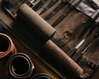 May include: A brown leather roll with multiple slots for holding knives. The roll is unrolled and the knives are visible. The roll is made of a thick, durable leather and has a zipper closure.