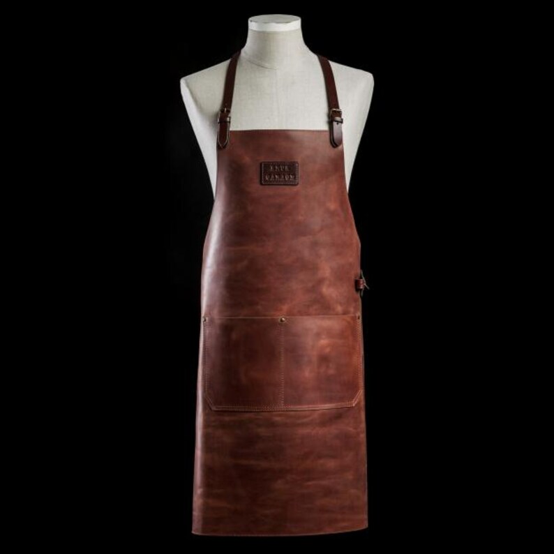 May include: A brown leather apron with adjustable straps and a large pocket. The apron has the text "TRUE NORTH" embossed on the front.