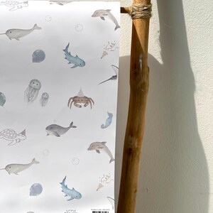 May include: White paper with a watercolor pattern of sea creatures, including whales, sharks, and jellyfish. The design features a light blue and gray color palette with party hats and bubbles. The text "LITTLE ROGLETS" and a website address are visible.