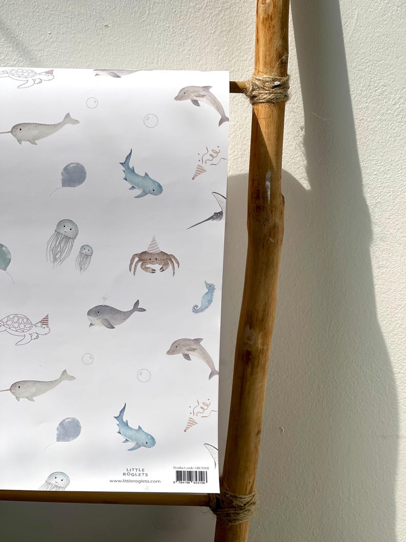 May include: White paper with a watercolor pattern of sea creatures, including whales, sharks, and jellyfish. The design features a light blue and gray color palette with party hats and bubbles. The text "LITTLE ROGLETS" and a website address are visible.