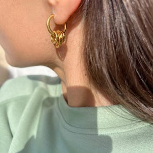 May include: Gold hoop earrings with multiple interlocking rings. The earrings are worn in a person's ear.