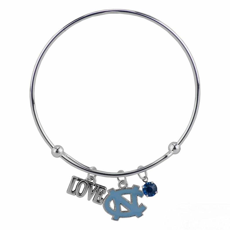 May include: A silver bangle bracelet with three charms. The charms include the word "LOVE" in silver, a light blue and silver emblem, and a blue gemstone. The bracelet is a simple, elegant design.