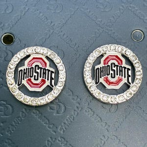 May include: Two circular Ohio State University logo charms featuring a red and white enamel center with the text OHIO STATE in black, surrounded by a border of clear, sparkling rhinestones set in a silver-toned metal frame.