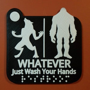 May include: Black and white bathroom sign with a werewolf and a bigfoot silhouette. The sign reads "Whatever Just Wash Your Hands" with braille dots below the text.
