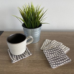 May include: Four brown and white polka dot coasters with a white ceramic mug with a brown interior on top of one of the coasters. A potted green plant is in the background.