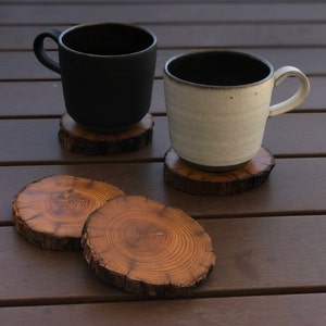 May include: Two ceramic mugs, one black and one white, are sitting on wooden coasters. The coasters are made from tree rounds and have a natural wood finish.