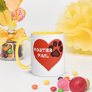 Peut inclure: Une tasse en céramique blanche avec un bord jaune. La tasse a un cœur rouge avec une empreinte de patte noire dessus. Le texte "Foster Fail" est écrit en lettres blanches à l'intérieur du cœur.