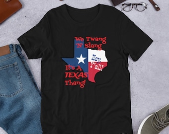 May include: Black t-shirt with a Texas-shaped graphic featuring a red, white, and blue flag design. The text "We Twang 'N' Slang It's A TEXAS Thang! Hey Y'all!" is printed on the shirt.