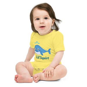 May include: A yellow baby onesie with a blue whale graphic and the text "Lil' Squirt".
