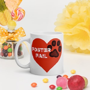 Peut inclure: Une tasse en céramique blanche avec un cœur rouge et une empreinte de patte noire. Le texte "Foster Fail" est imprimé en lettres blanches sur le cœur.