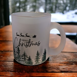 May include: White frosted mug with a black silhouette of Santa Claus and reindeer flying over a snowy forest. The mug says "Merry Christmas" in black lettering.