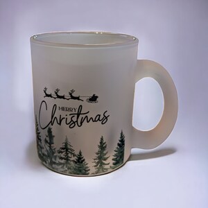 May include: White frosted ceramic mug with a black and green design. The design features a silhouette of Santa Claus in a sleigh pulled by reindeer with the text "Merry Christmas" and a row of pine trees.