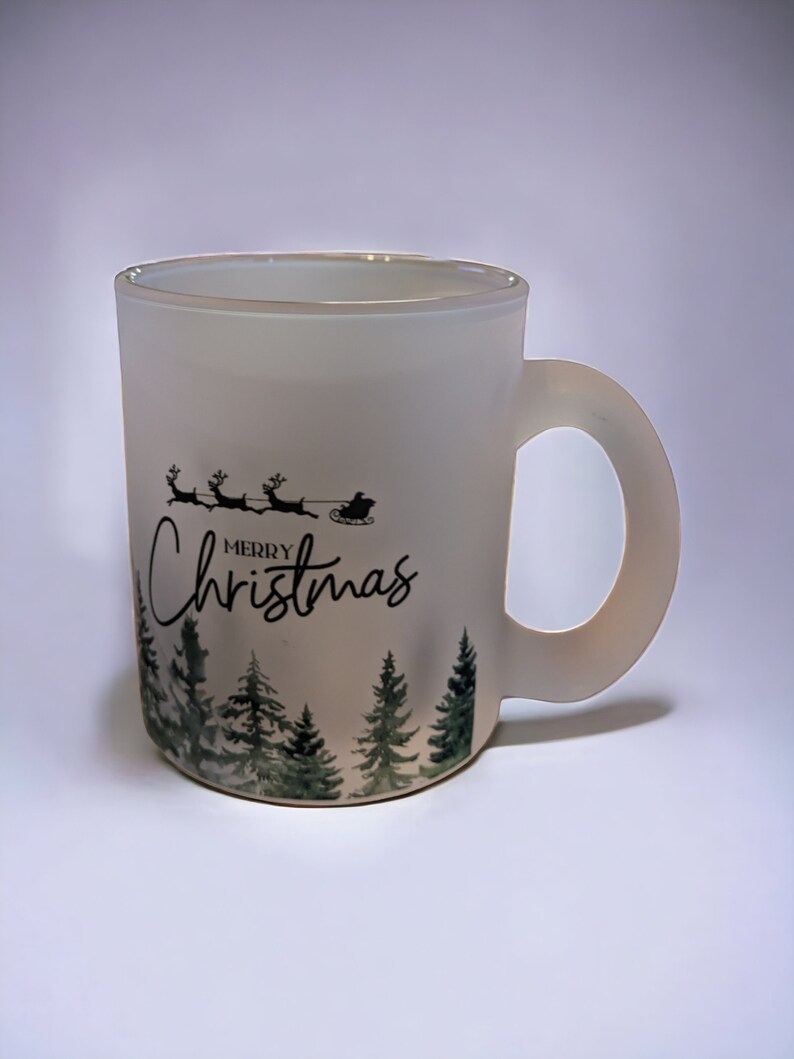 May include: White frosted ceramic mug with a black and green design. The design features a silhouette of Santa Claus in a sleigh pulled by reindeer with the text "Merry Christmas" and a row of pine trees.