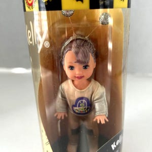 May include: A Kelly doll in a clear plastic container. The doll is dressed in a Halloween costume, with a silver headband and antennae. The packaging has the words "Special Edition" and "Halloween party".