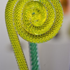 May include: A yellow glass sculpture with a spiral design. The sculpture is made of twisted glass rods and has a smooth, shiny finish.