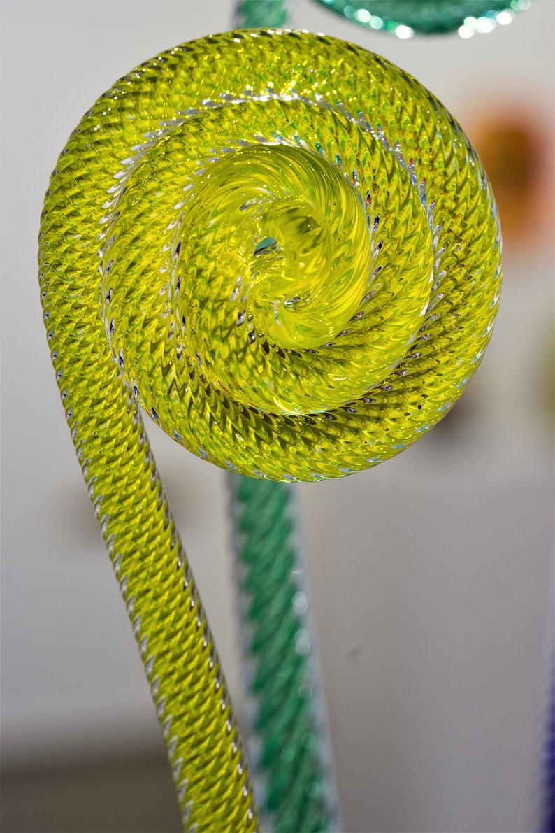 May include: A yellow glass sculpture with a spiral design. The sculpture is made of twisted glass rods and has a smooth, shiny finish.