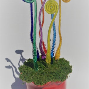 May include: A rainbow-colored glass sculpture of fern-like plants in a red pot with green moss. The sculpture is made of glass and is a unique and colorful piece of art.