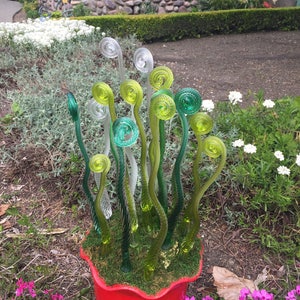 May include: A red ceramic planter with a green moss-like lining and a cluster of glass fern sculptures in shades of green and clear.