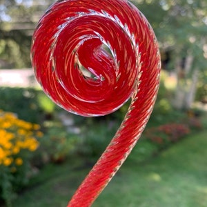 May include: A red glass spiral, twisted and curled, with a clear glass finish. The spiral is a decorative element for a garden or home.