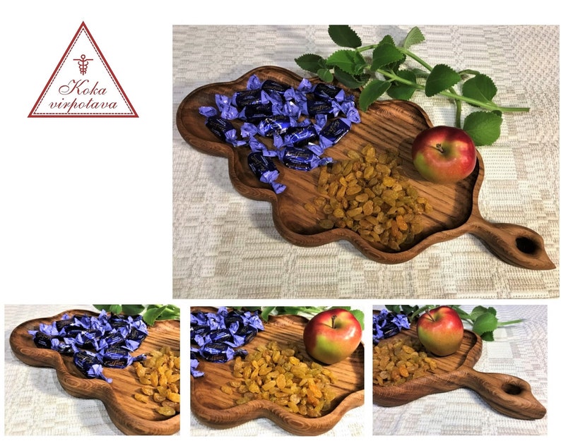 May include: A wooden serving tray shaped like a leaf with a handle. The tray is filled with purple candies, yellow raisins, and a red apple.